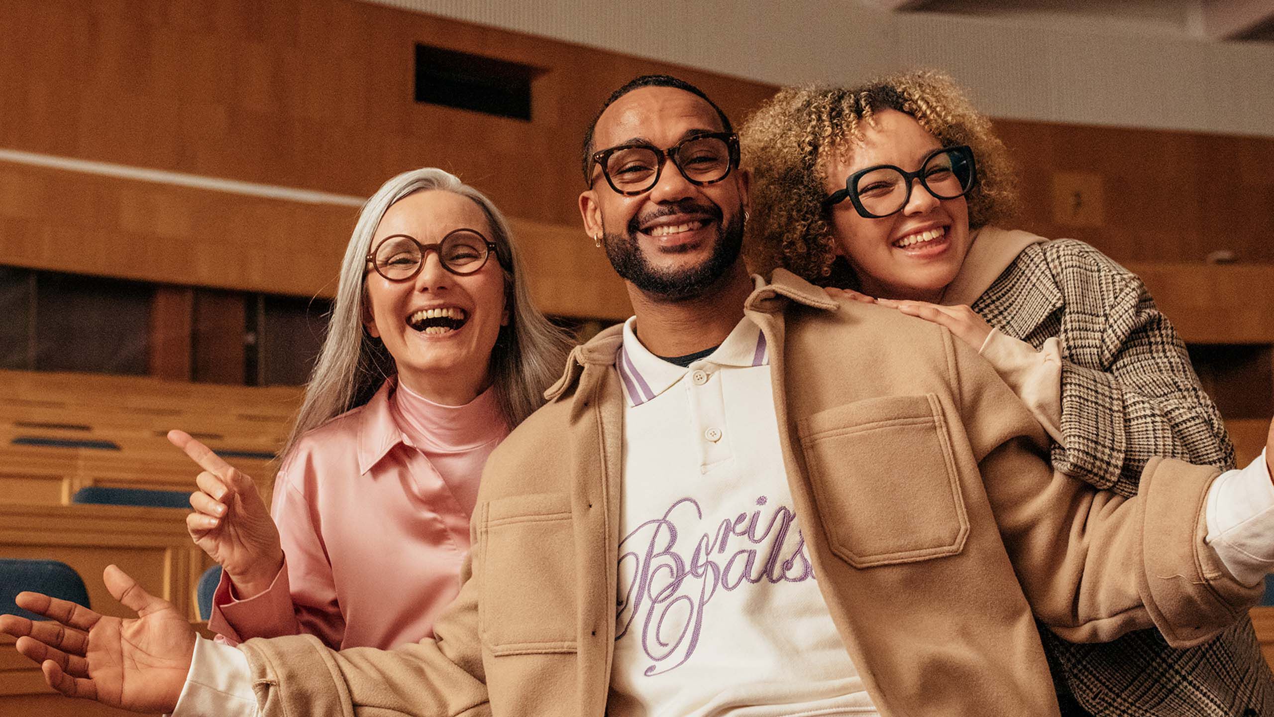 Mies ja kaksi naista poseeraavat iloisina ryhm&auml;kuvassa luentosalissa