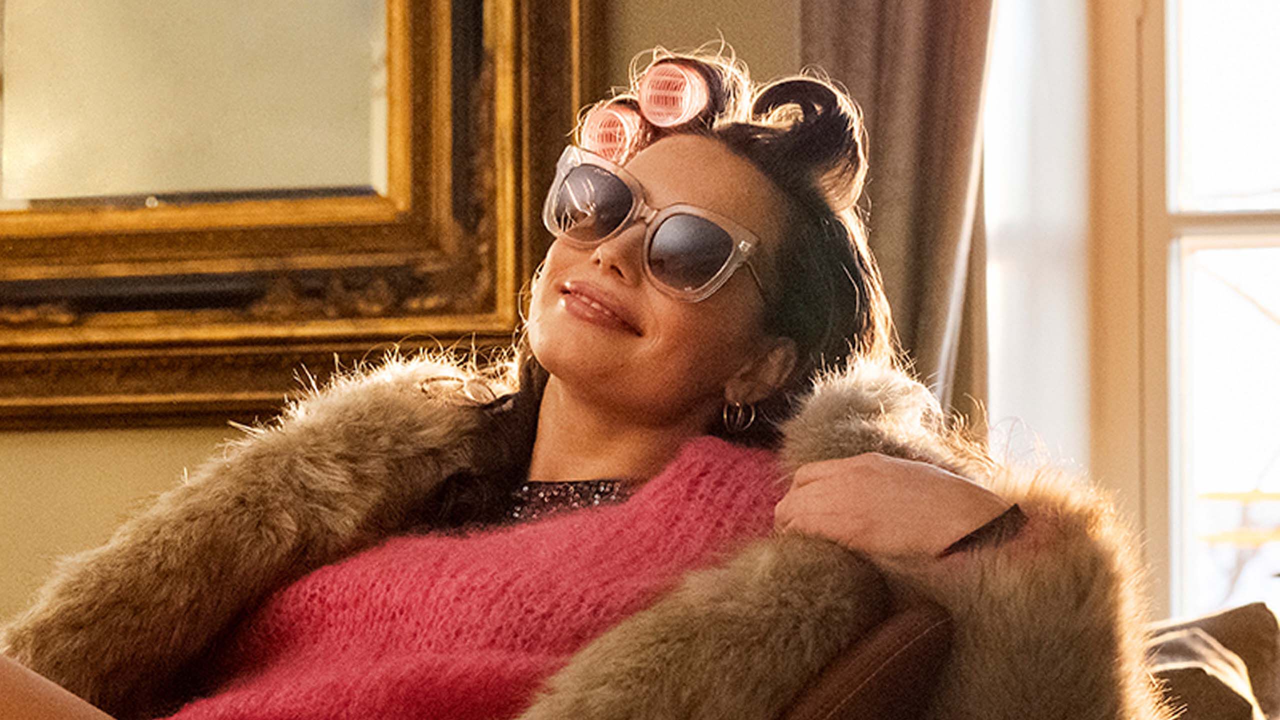 Nainen istuu rennosti tuolilla, jalat p&ouml;yd&auml;n p&auml;&auml;ll&auml;, aurinkolasit ja takki yll&auml;&auml;n