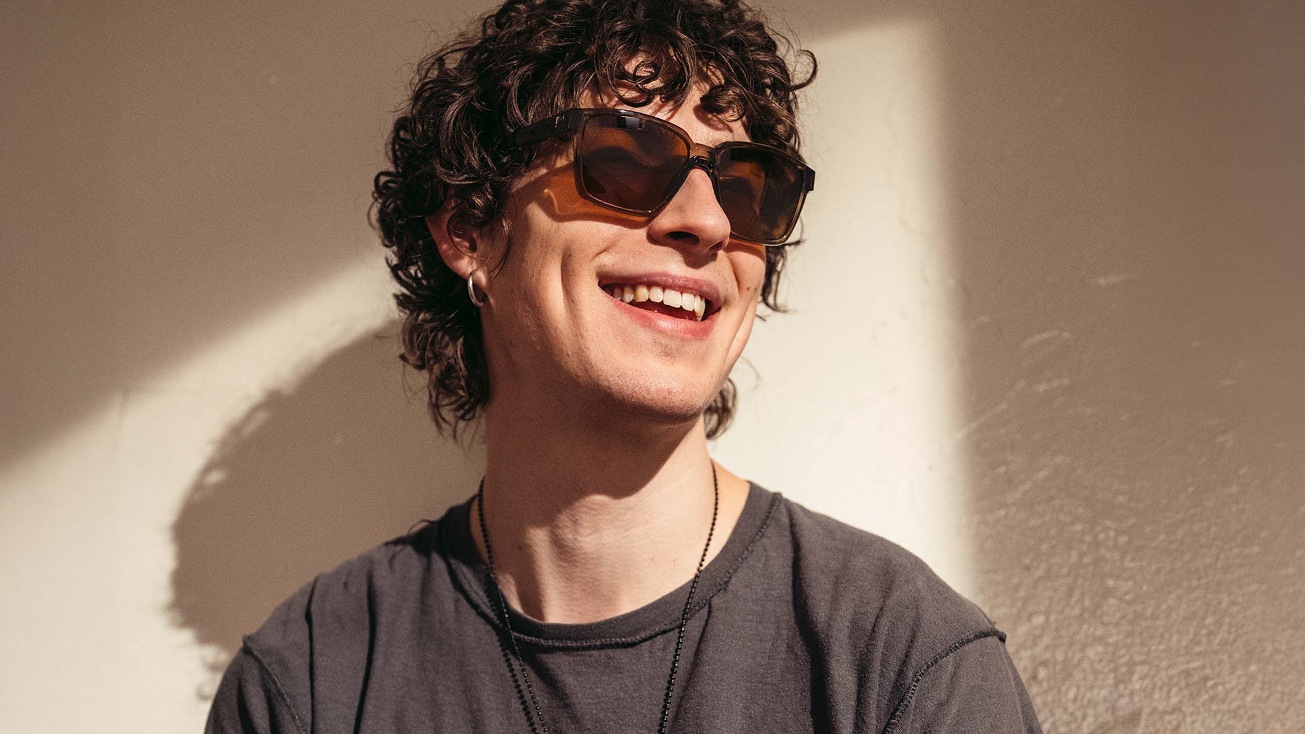 Nuori mies hymyilee aurinkolasit silmill&auml;.