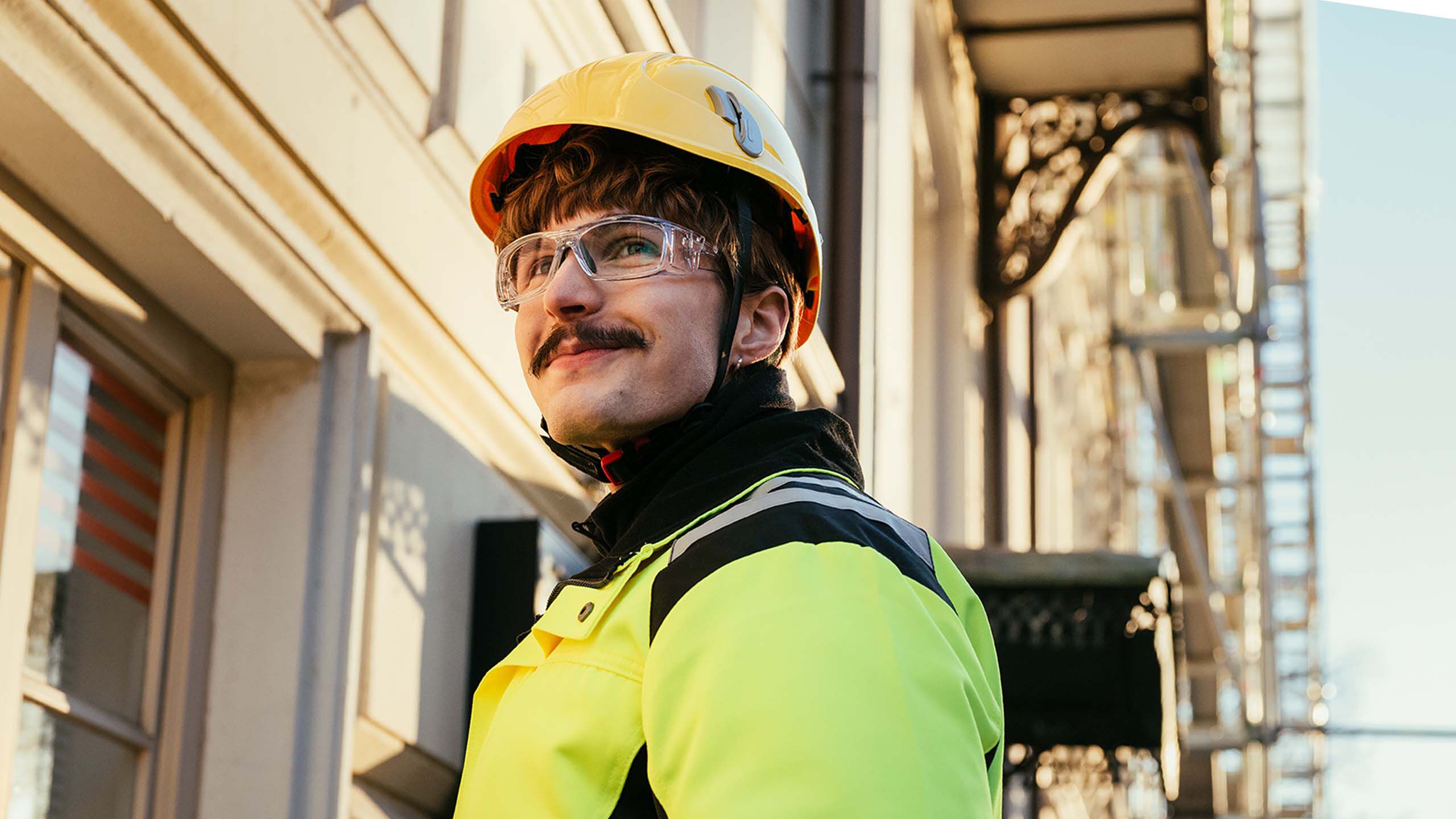 Rakennusmies hymyilee ty&ouml;maalla suojalasit kasvoillaan.