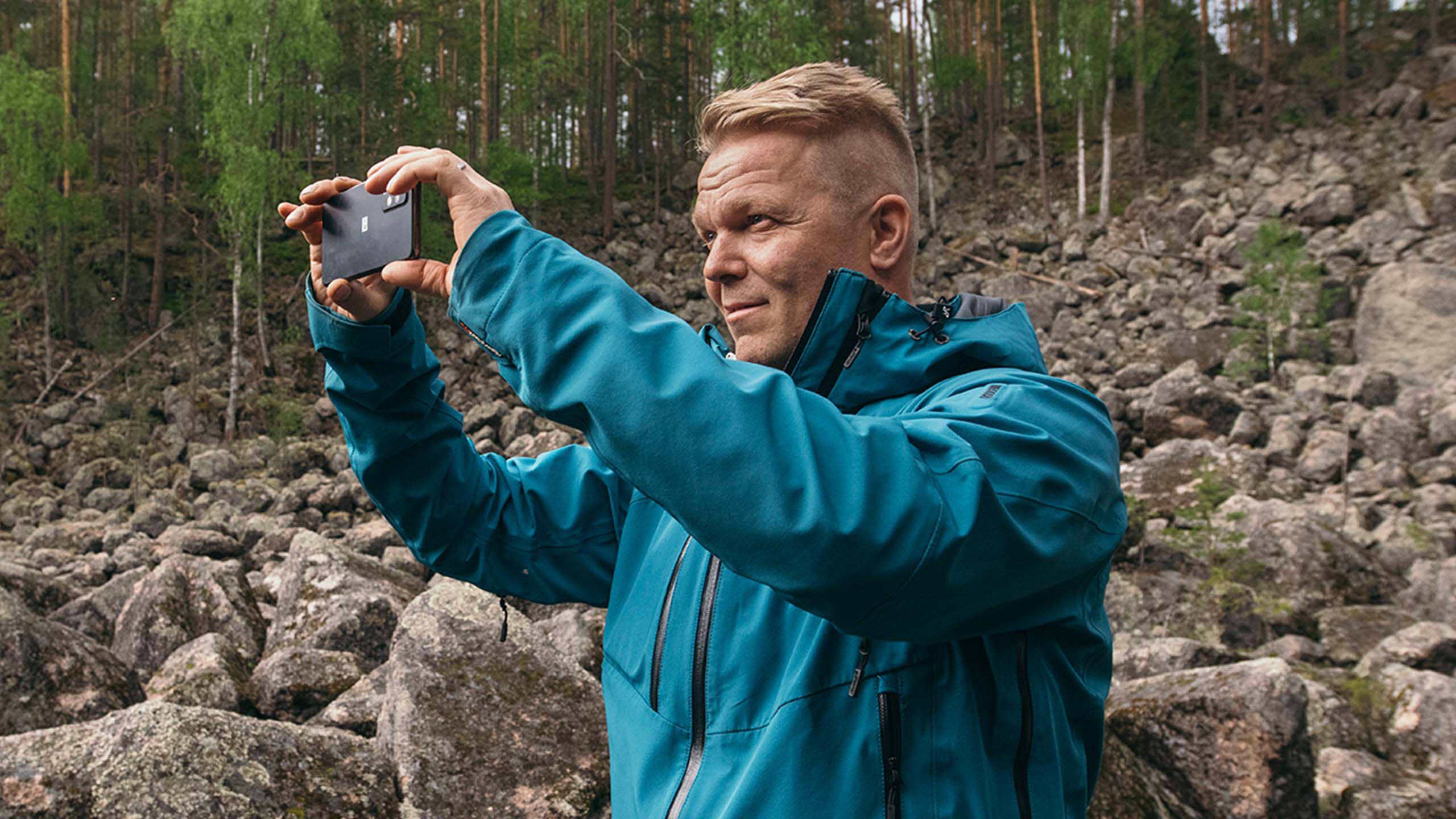 Keski-ik&auml;inen mies ilman silm&auml;laseja ottaa kuvaa puhelimella.