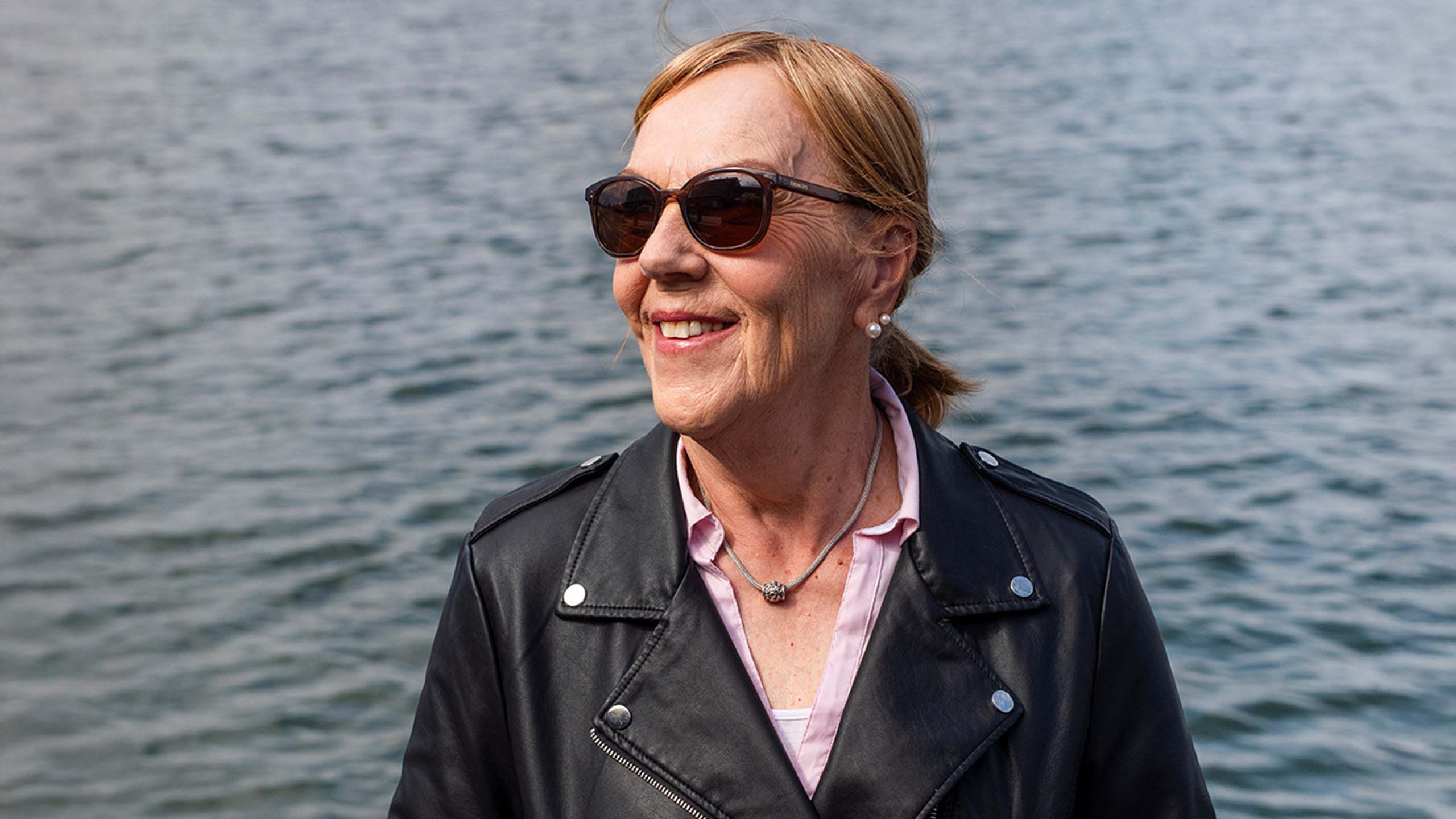 Vanhempi nainen meren rannassa aurinkolasit kasvoilla.