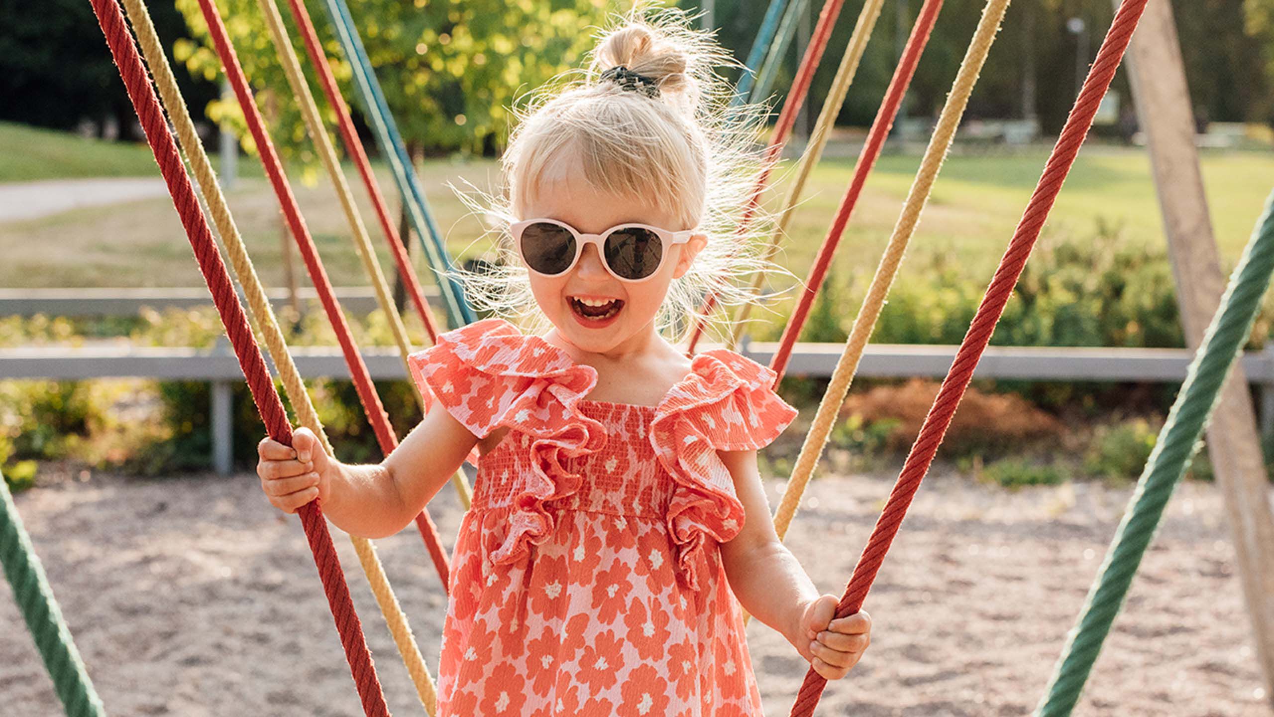 Pieni lapsi leikkii kiipeilytelineess&auml;, vaaleanpunaiset aurinkolasit kasvoilla.