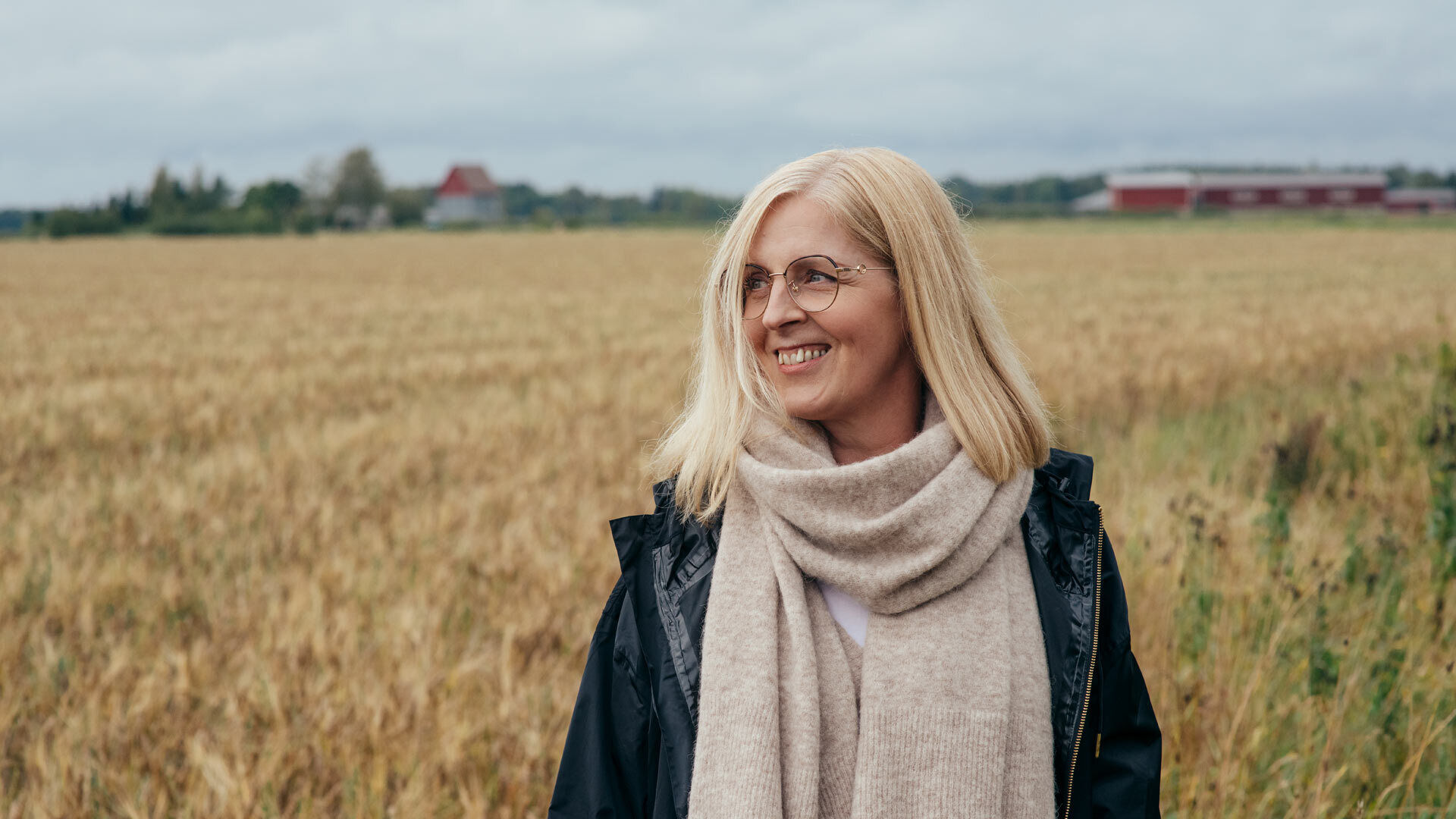 Rouva seisoo pellon reunassa, kasvoilla py&ouml;re&auml;t metalliset silm&auml;lasit