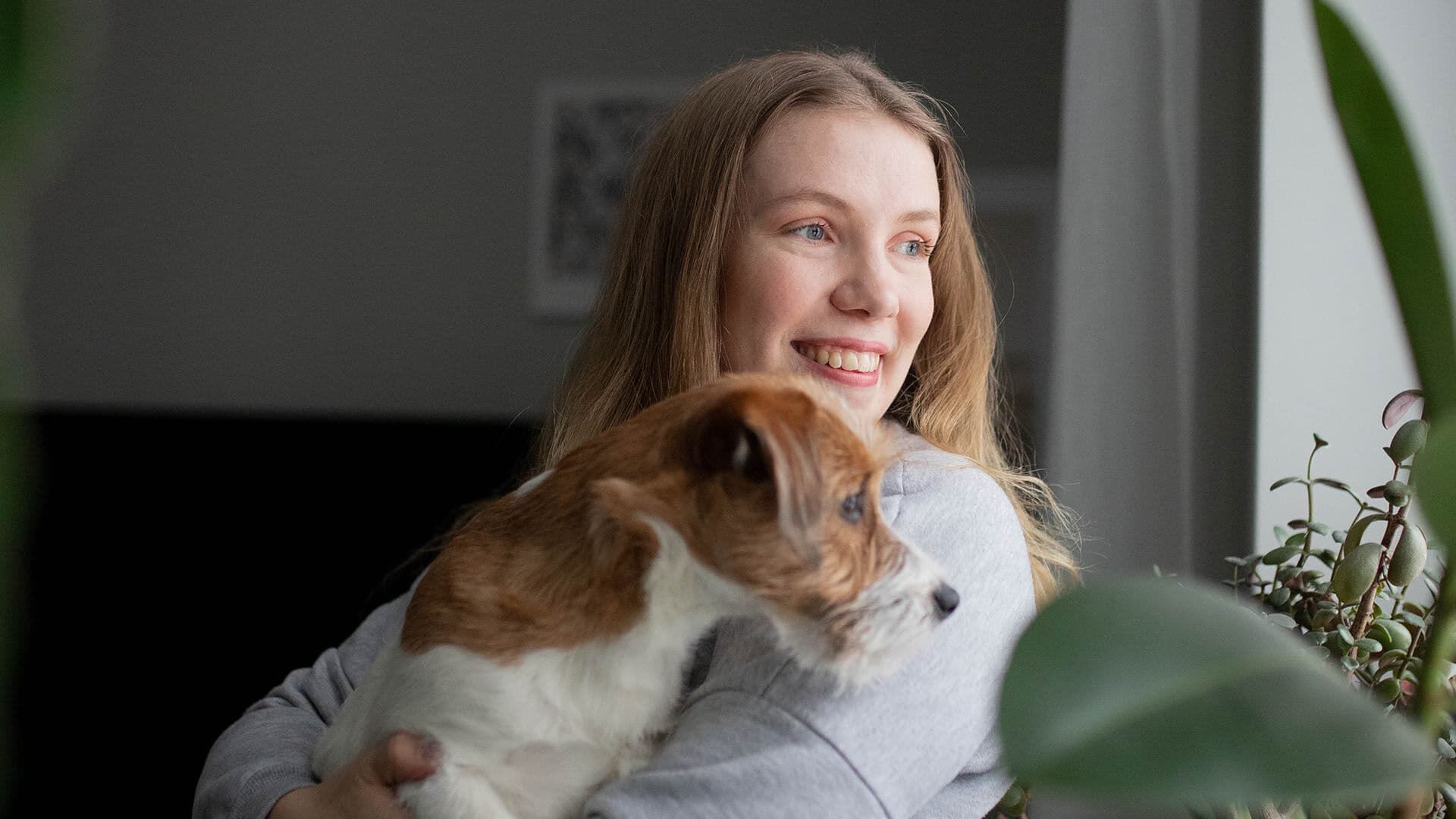  Somevaikuttaja Tiia Suomalainen katsoo koira syliss&auml;&auml;n ulos ikkunasta