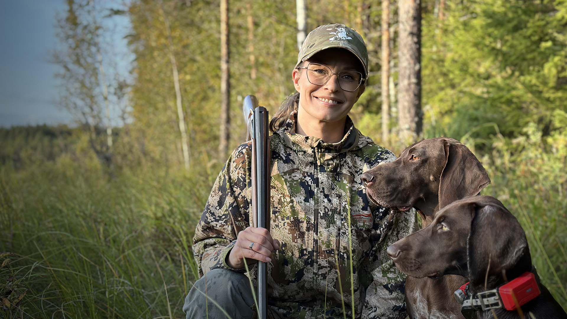 Mets&auml;st&auml;j&auml; kahden koiran kanssa pellon reunalla