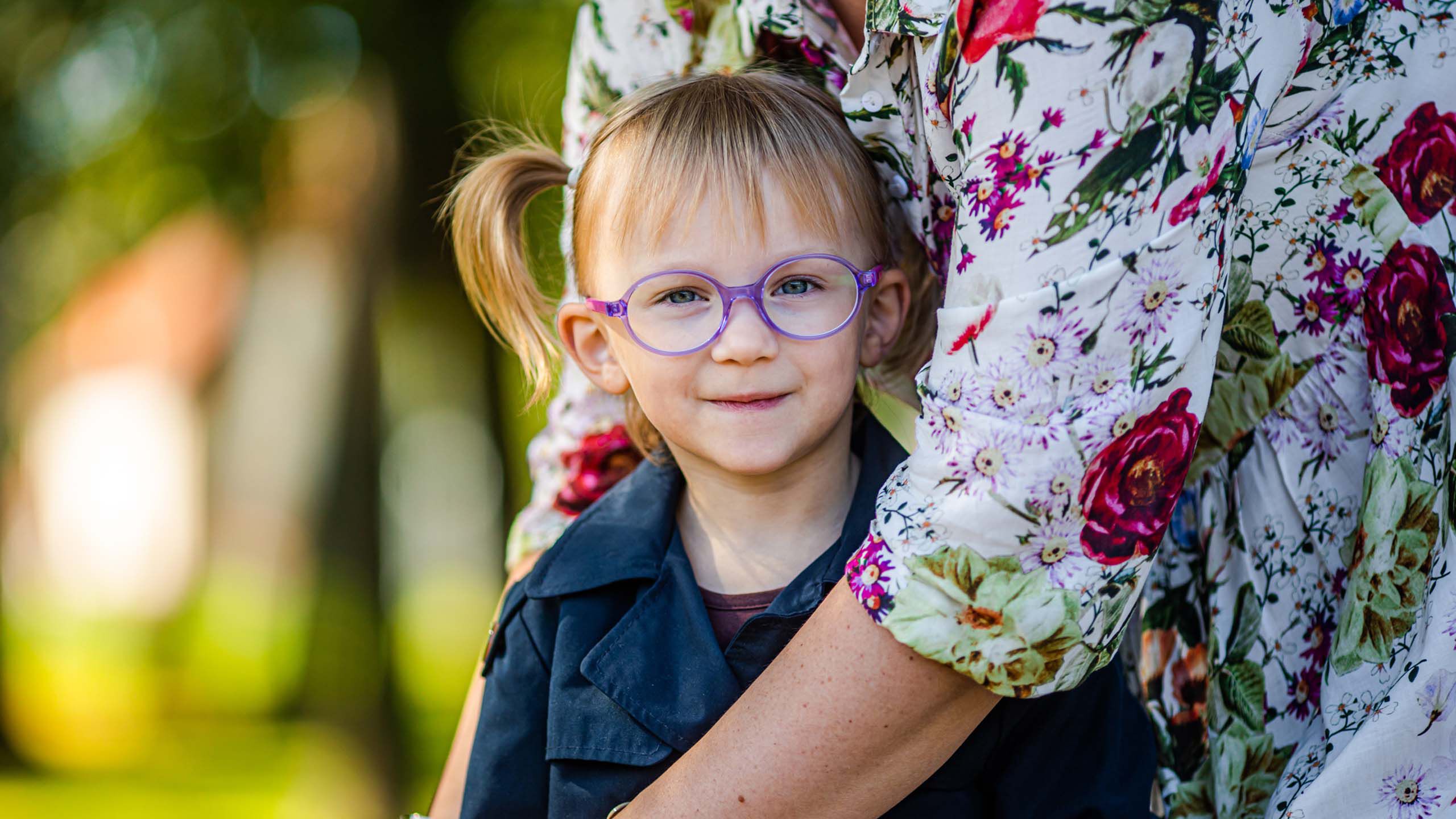 Lapsi violetit silm&auml;lasit kasvoilla halaa aikuista.