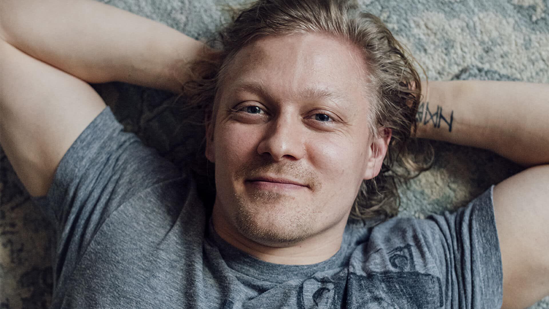 Mies hymyilee ja makaa maton p&auml;&auml;ll&auml;