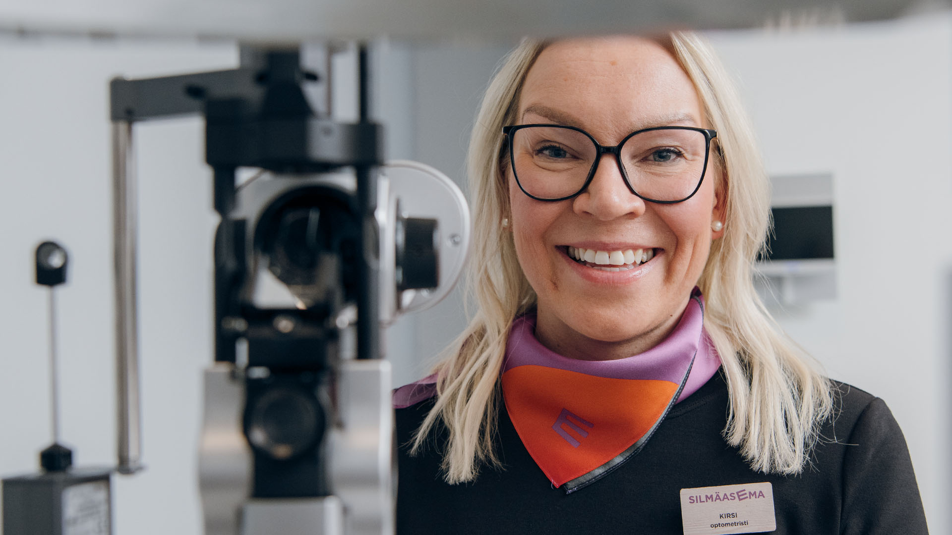 Iloinen optikko näöntutkimuslaitteen takana