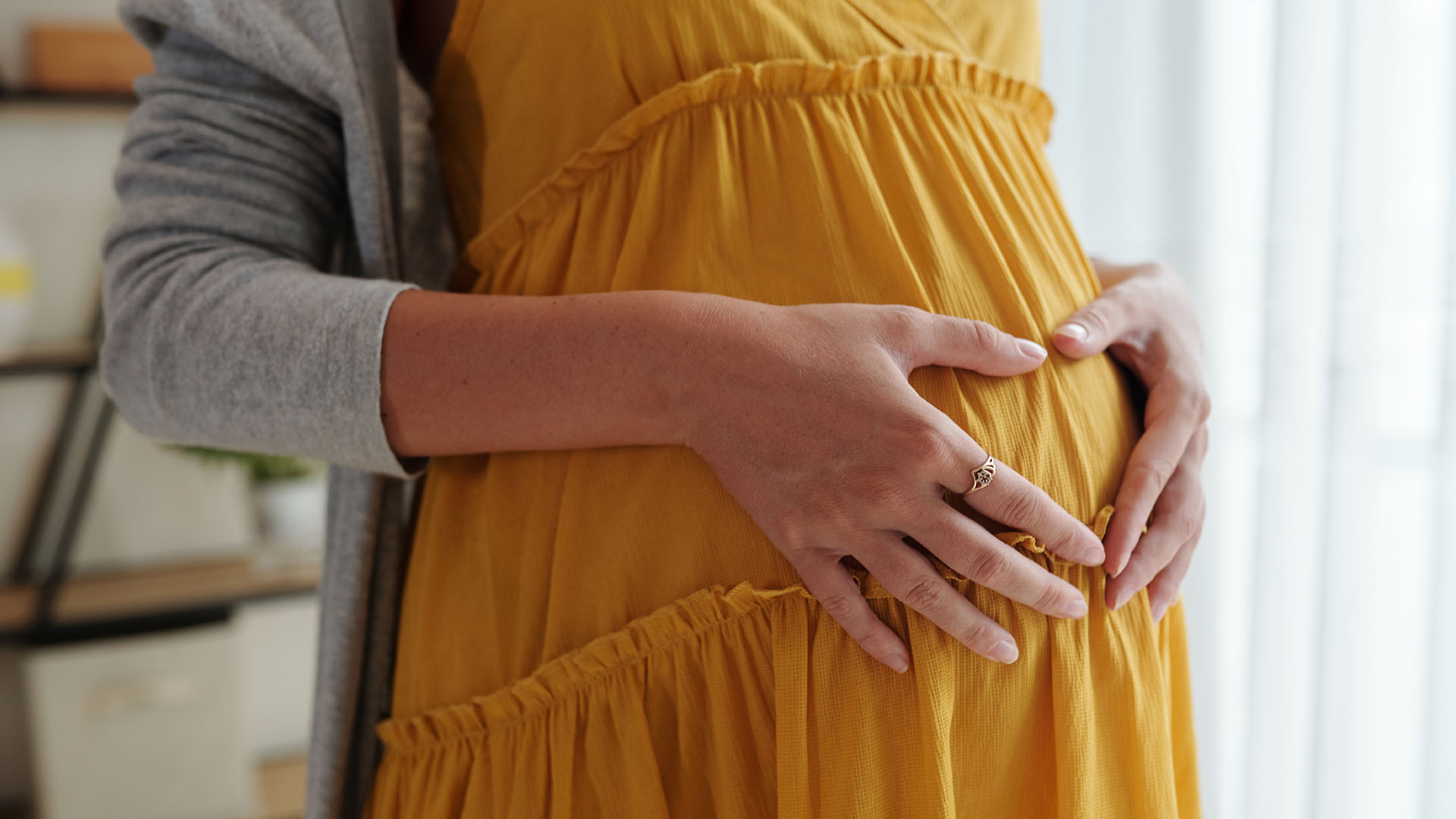 Keltamekkoisen raskaana olevan naisen vatsa ja käsillä muodostettu sydän