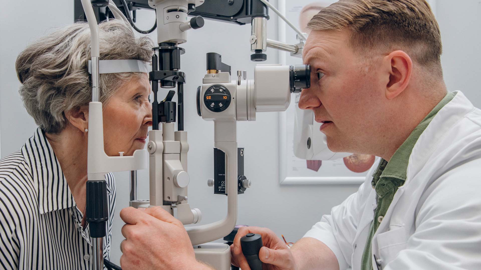 Silmälääkäri tutkii kaihi-ikäisen rouvan silmiä mikroskoopilla
