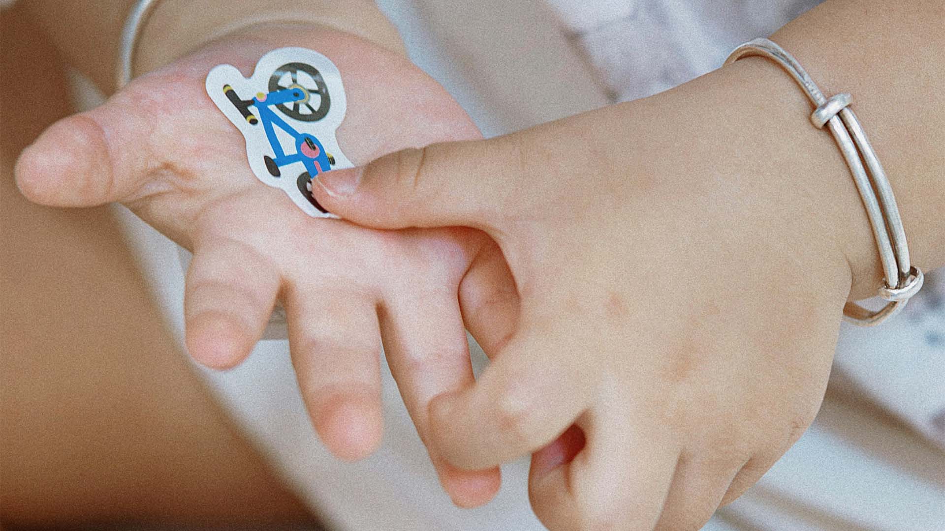 Lapsen kädet ja palkinnoksi saatu tarra liimattuna kämmenelle.