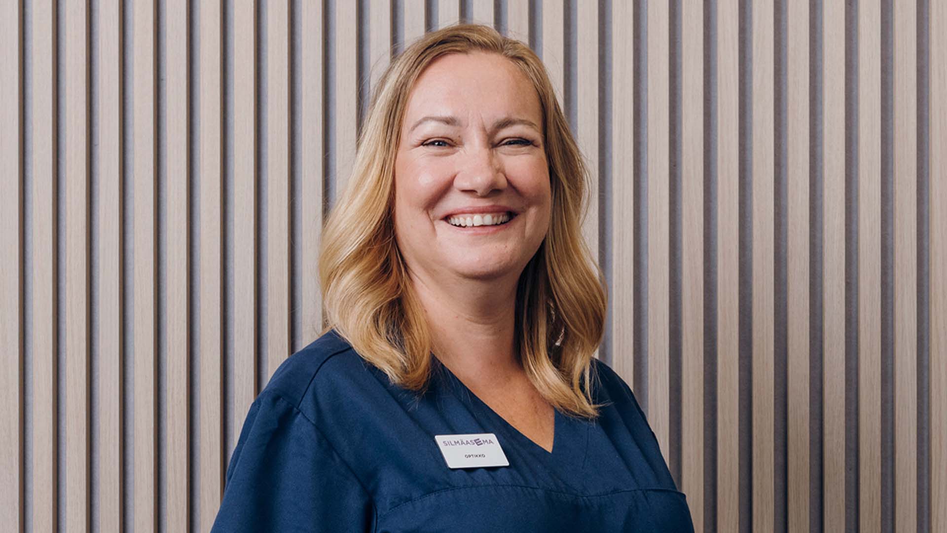 Silmäsairaalan optikko rimaseinän edessä kameralle hymyillen