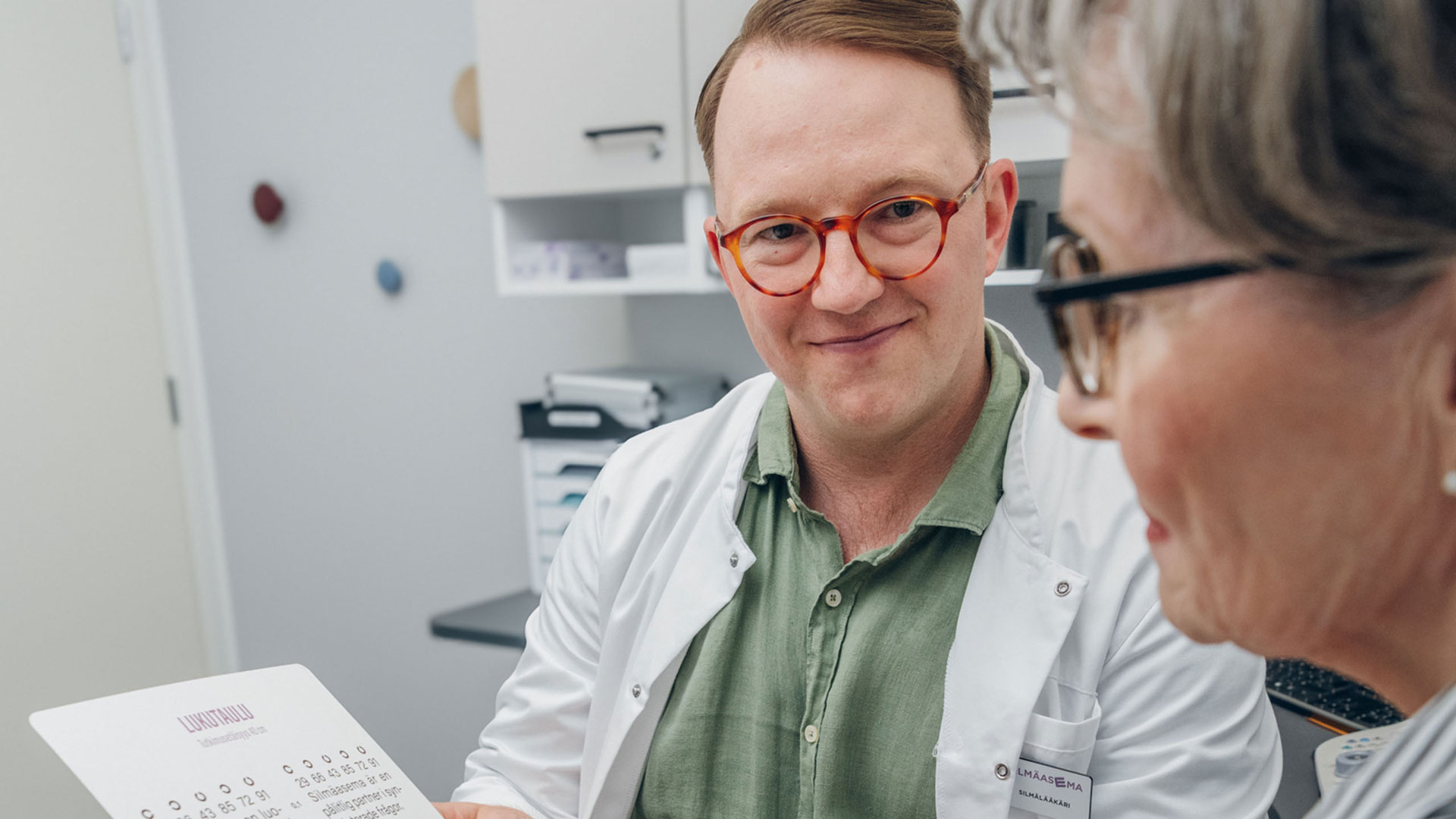 Silmälääkäri tutkimushuoneessa asiakkaan kanssa
