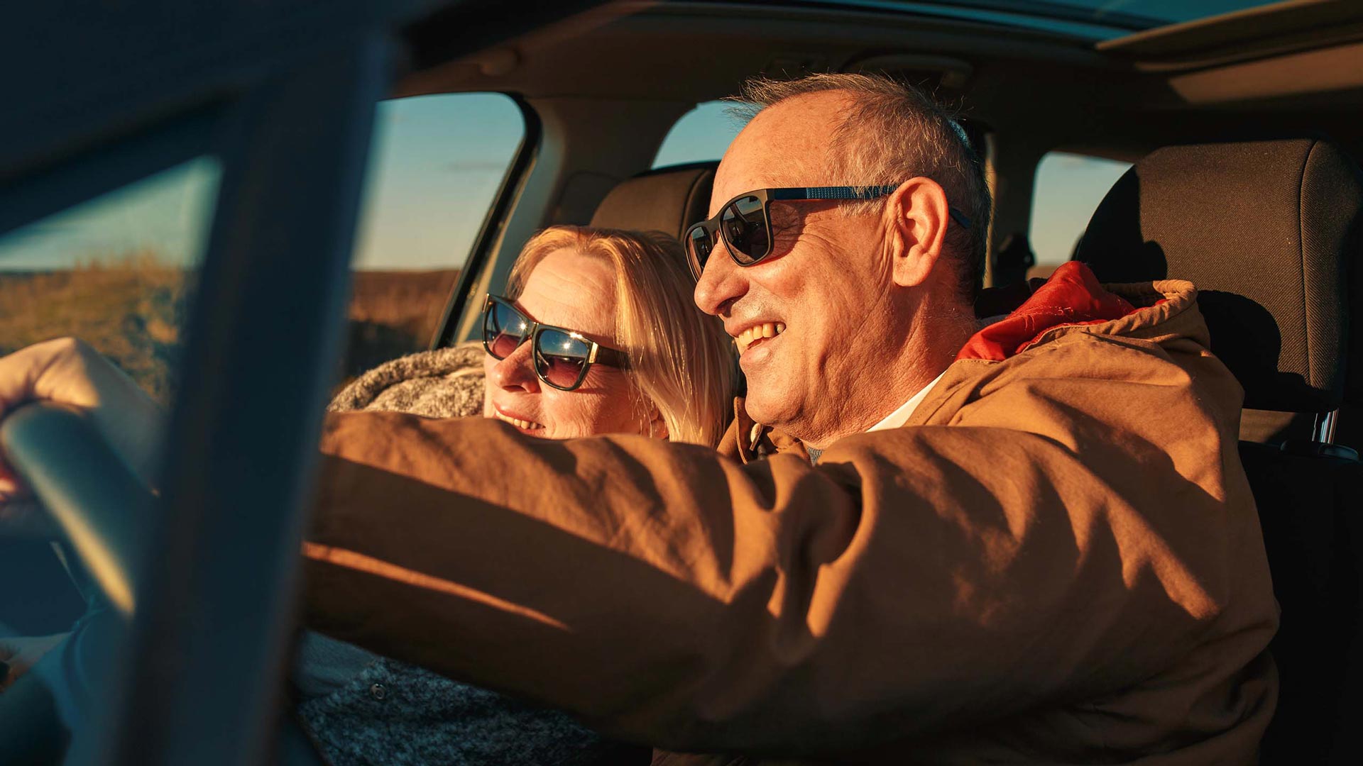 Aurinkolasit päässä autossa istuvat mies ja nainen