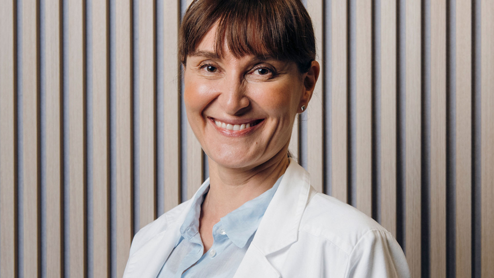 Ystävällinen silmälääkäri hymyilee kameralle rimaseinän edessä