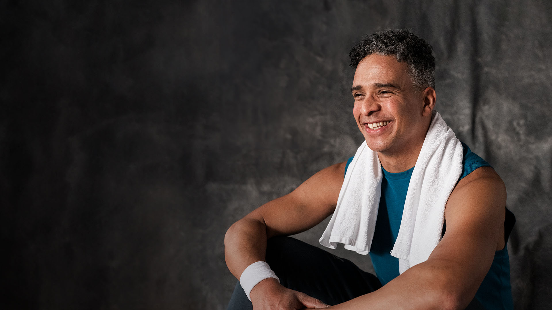 Mies istuu lattialla treenien jälkeen pyyhe olalla