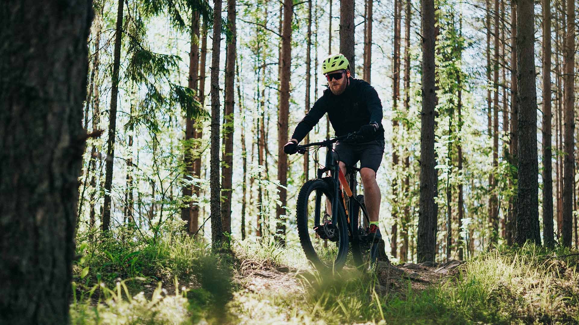 Maastopyöräilijä metsässä urheiluaurinkolasit päässä.
