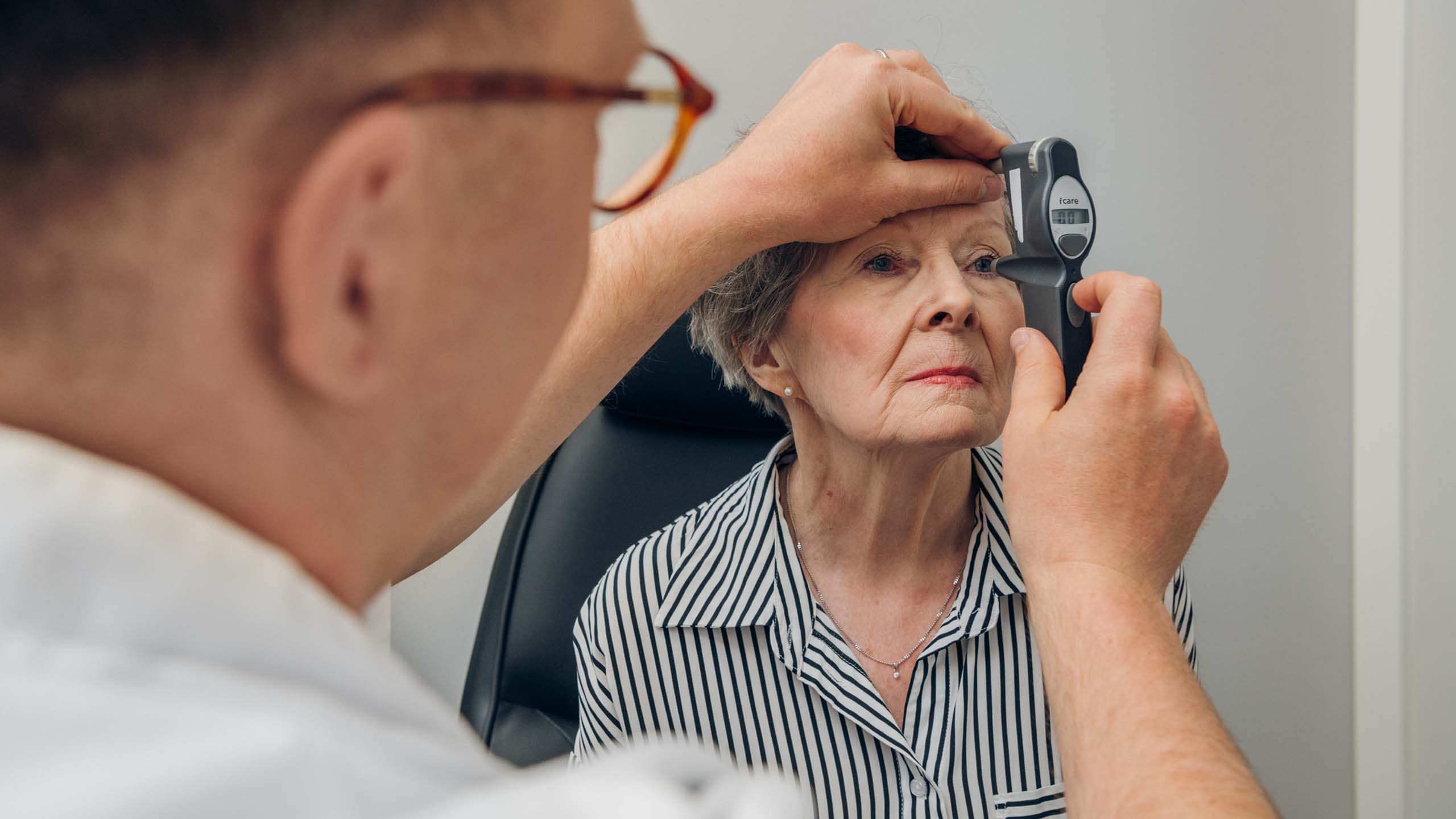 Vanhempi rouva mittauttaa silmänpainetta lääkärin vastaanotolla