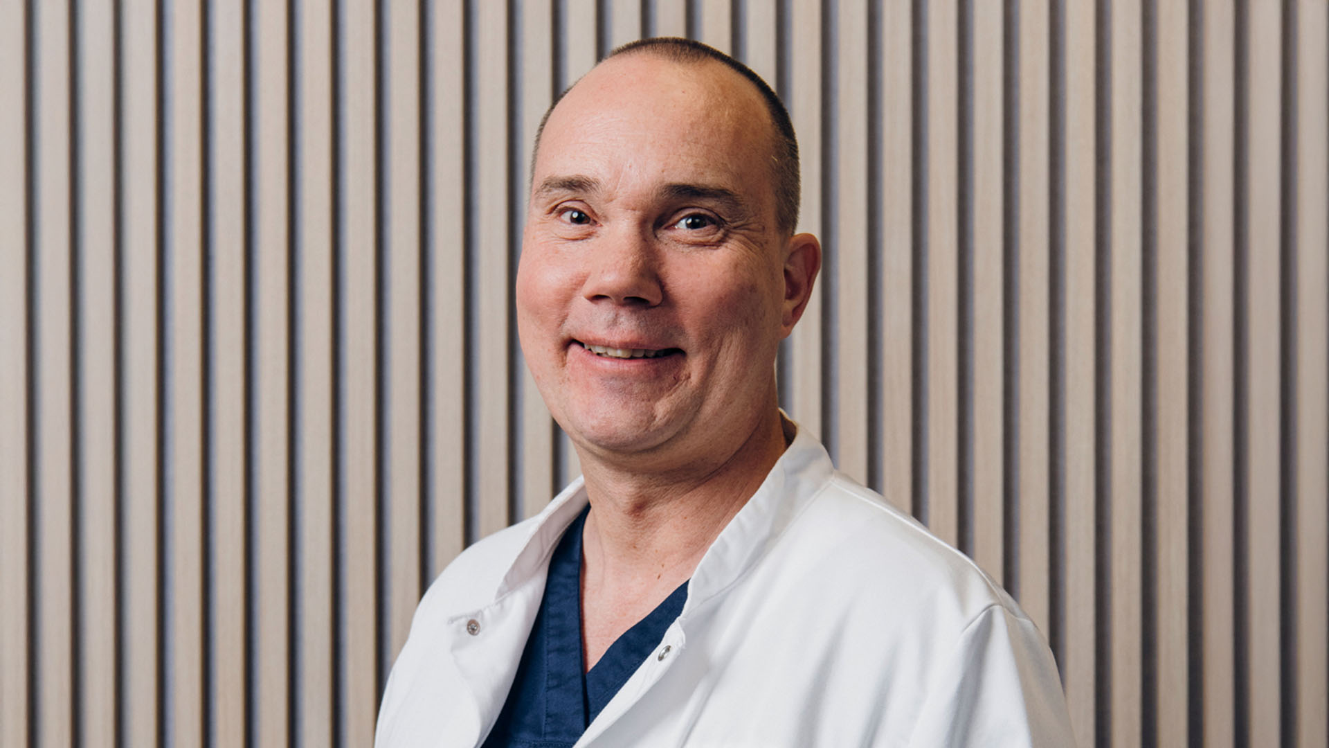 Silmälääkäri hymyilee tutkimuslaitteen takana kameralle