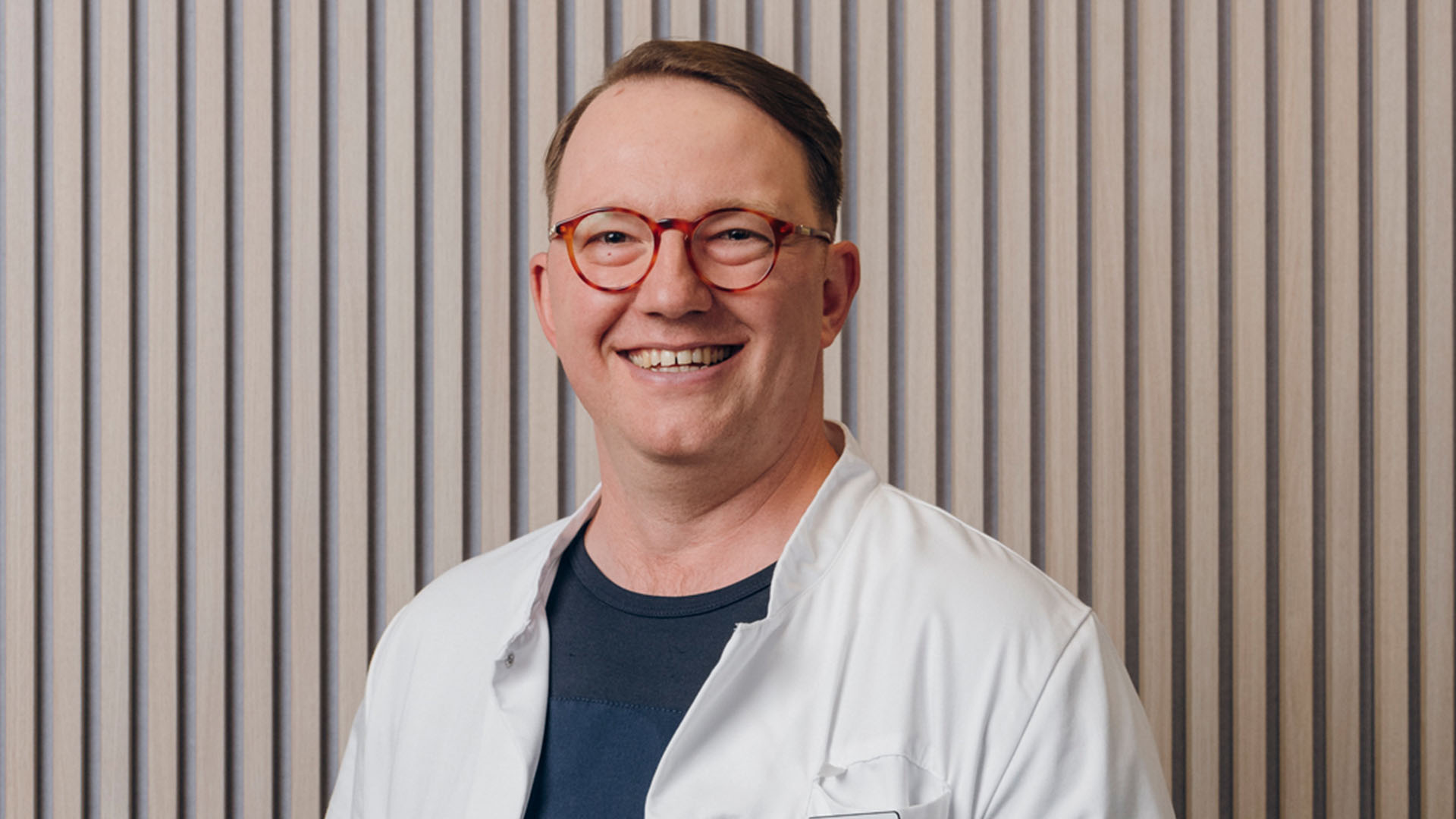 Silmälääkäri hymyilee kameralle rimaseinän edessä