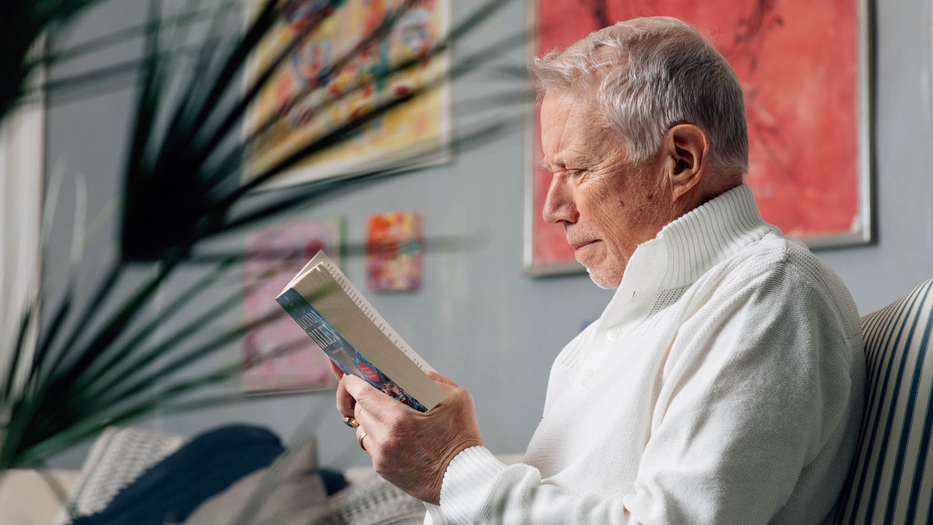 Kaihi-ikäinen mies lukee kirjaa sisätiloissa