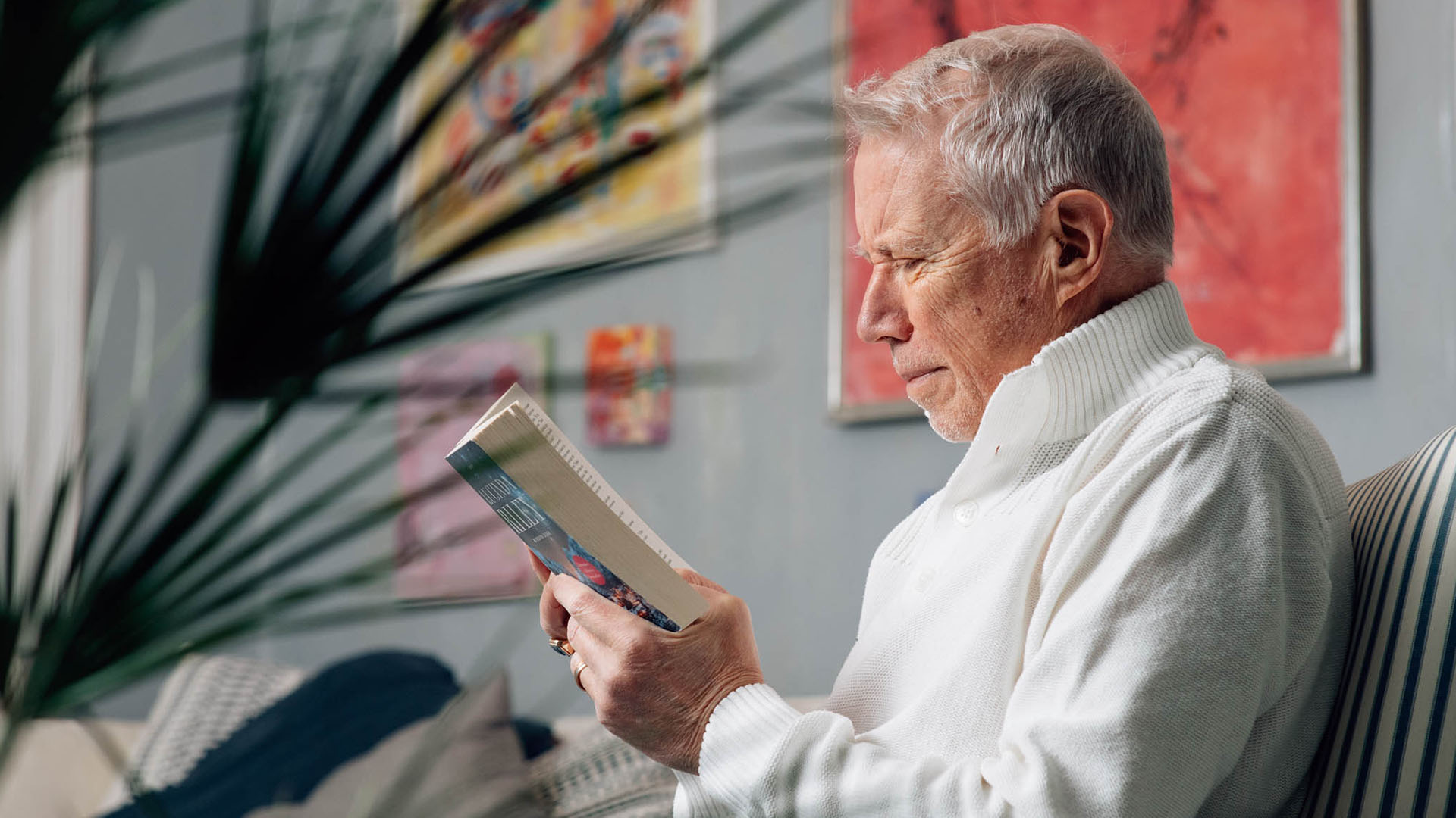 Kaihi-ikäinen mies lukee kirjaa sisätiloissa