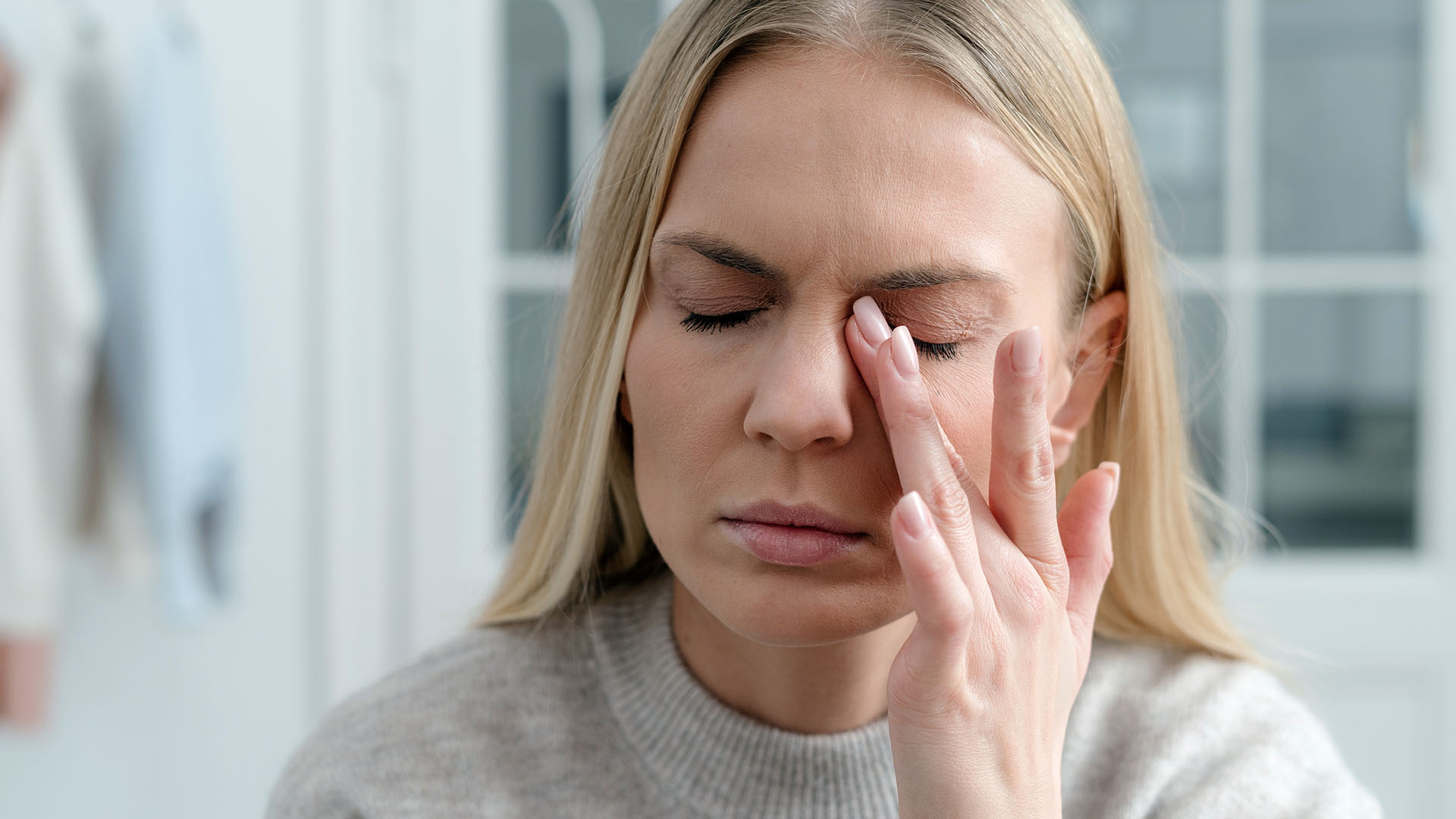 Silmätulehduksen oireista kärsivä nainen painaa suljettua silmää sormella