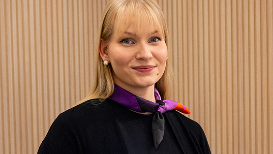 Optikko hymyilee kameralla myymälässä rimaseinän edessä