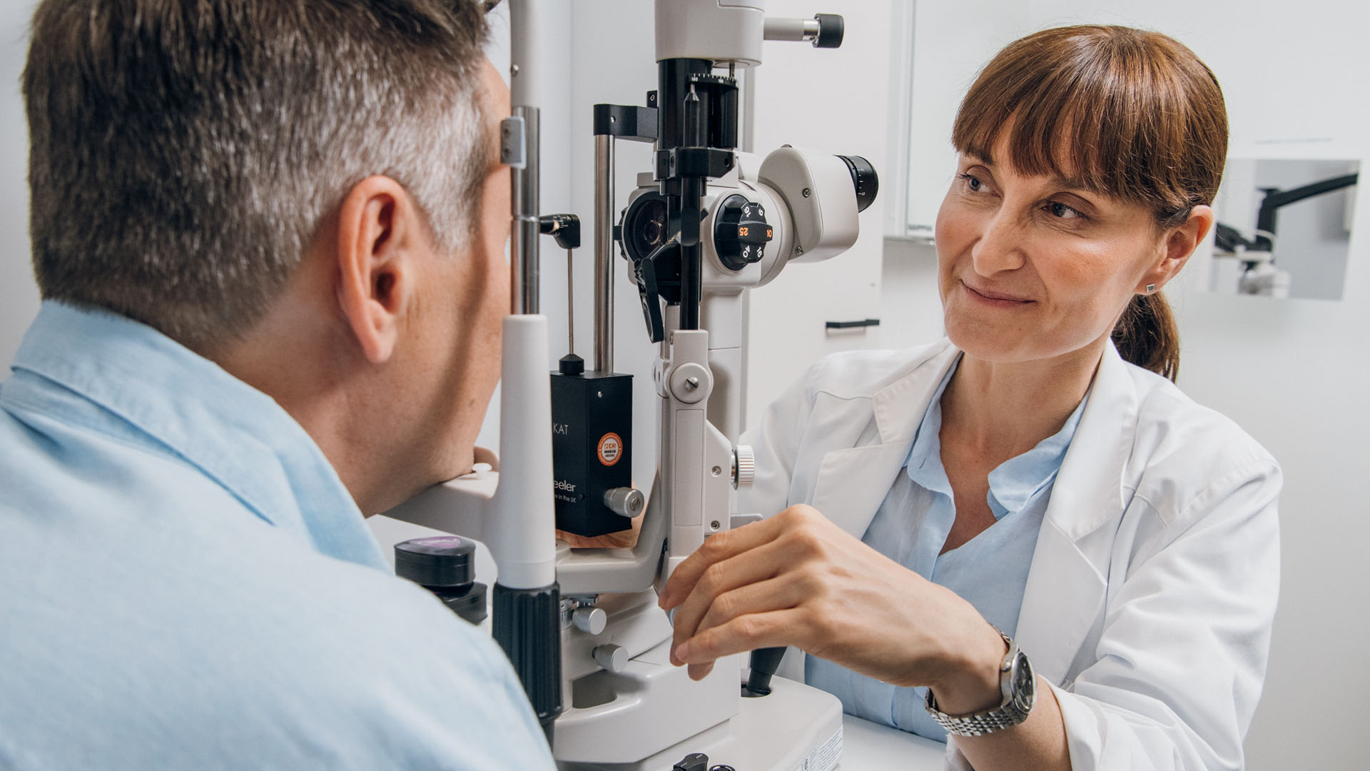 Silmälääkäri ja asiakas tutkimushuoneessa mikroskoopin takana