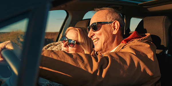 Aurinkolasit päässä autossa istuvat mies ja nainen